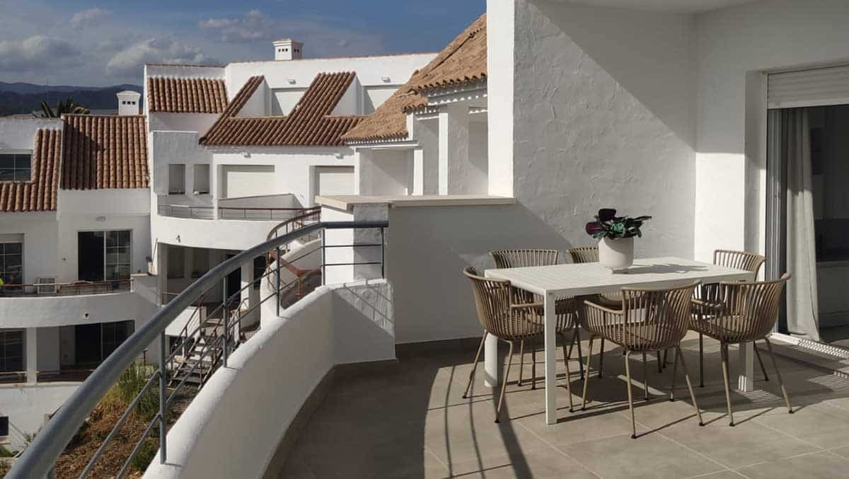 Modern balcony with dining set, overlooking white-washed villas and scenic hills in a sunny coastal location.